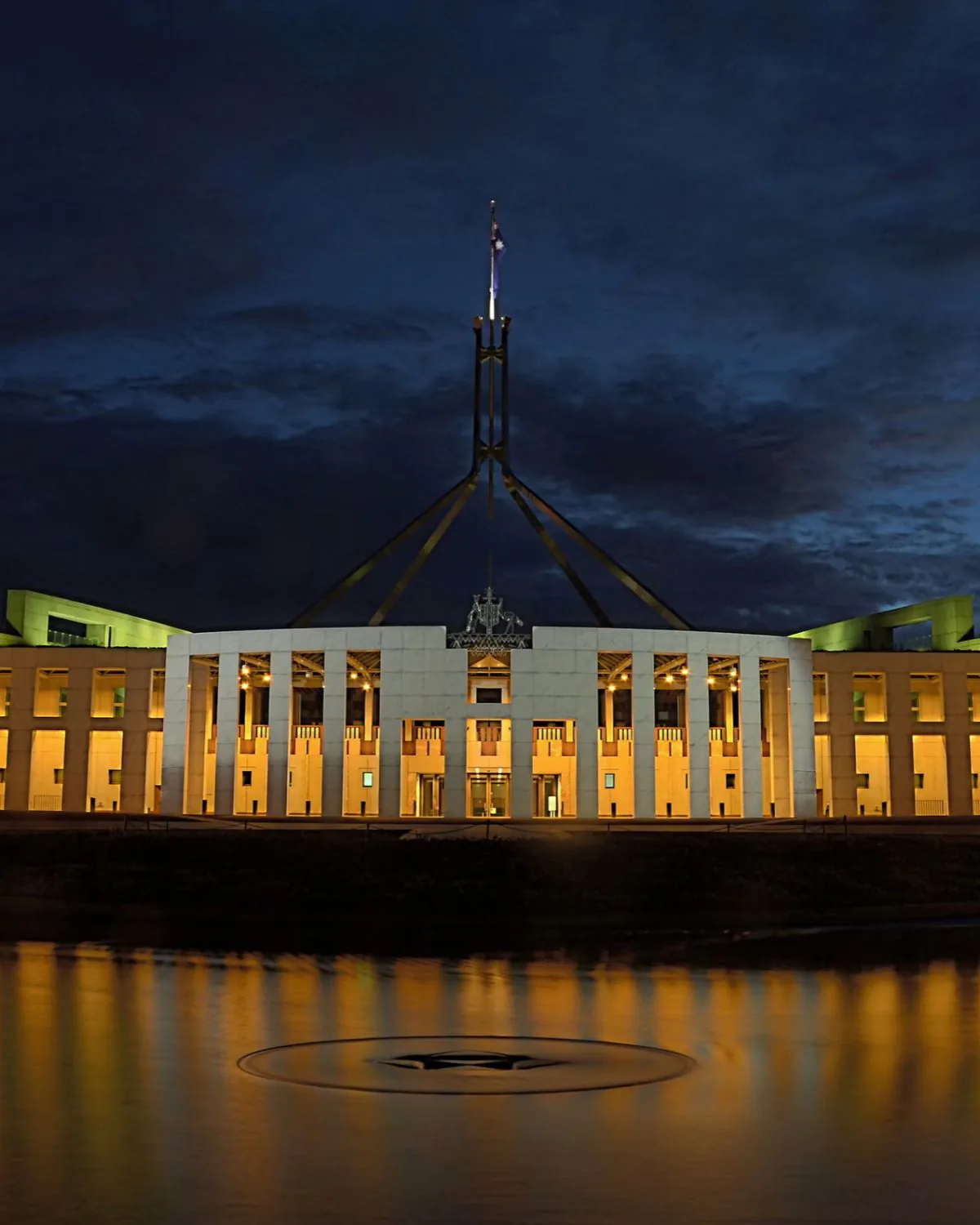 Parliament House in Canberra lit up at night, with its lights reflected in the water in front
